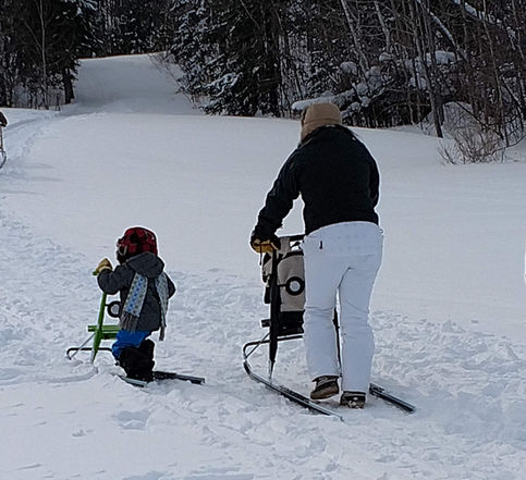A mom and child kick sledding in winter snow. 